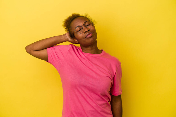 Mujer afroamericana joven aislada sobre fondo amarillo con dolor de cuello debido al estrés, masajeando y tocando con la mano. - Foto, imagen