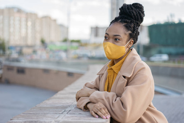 Afro saçlı, koruyucu yüz maskesi takan, sokakta bekleyen ve mekanı kopyalayan düşünceli Afro-Amerikan kadın. Sağlık, güvenlik yaşam tarzı konsepti - Fotoğraf, Görsel