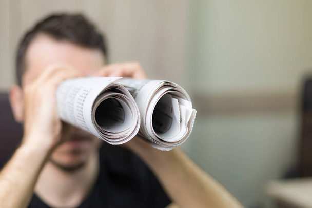 Man holding two twisted roll newspaper. Metaphor or allegory with binoculars. Selective focus on newspapers. Truth search concept - Fotó, kép