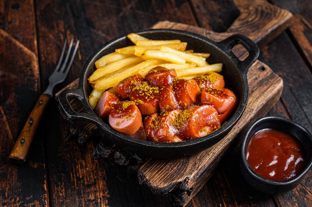 Currywurst street food meal, Curry spice on wursts served French fries in a pan. Dark wooden background. Top view - Photo, Image