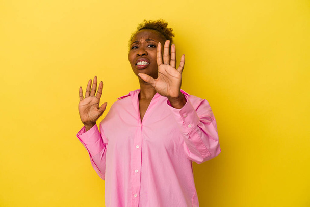Genç Afrikalı Amerikalı kadın, sarı arka planda izole edilmiş, tiksinti belirtisi gösteren birini reddediyor.. - Fotoğraf, Görsel