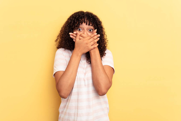 Young mixed race woman isolated on yellow background covering mouth with hands looking worried. - Fotografie, Obrázek