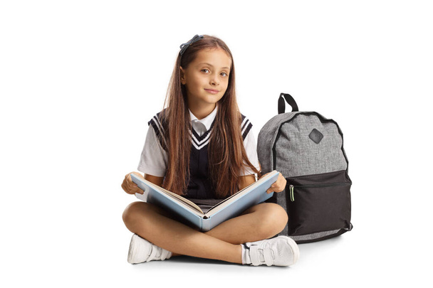 Schoolgirl sitting on the floor with a book on her lap isolated on white background - Photo, Image