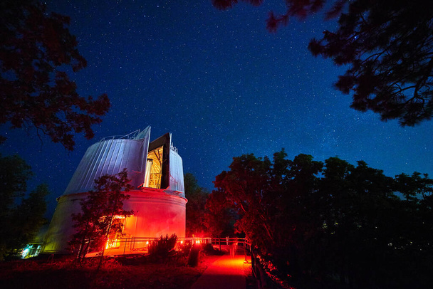 Krajobraz obserwatorium oświetlone w nocy czerwonymi i niebieskimi światłami z drzewami w tle - Zdjęcie, obraz