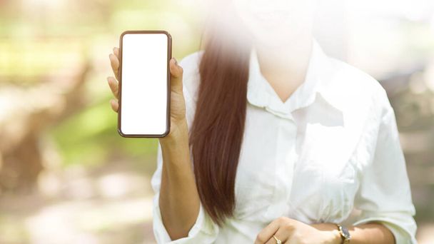 Mujer presenta una pantalla de teléfono inteligente en blanco a la cámara sobre un fondo borroso jardín. Mockup para su montaje gráfico. - Foto, imagen