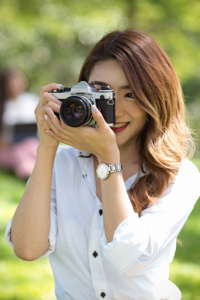 Приваблива молода жінка-туристка фотографує старовинну або ретро-камеру в зеленому парку. фотограф, мандрівник, блогер
. - Фото, зображення