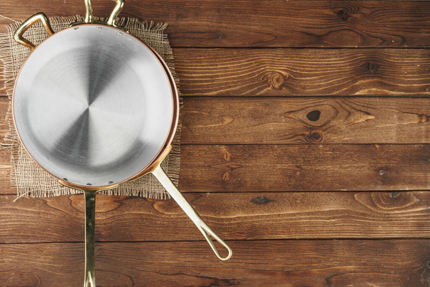 Copper frying pan on wooden background, top view - Фото, изображение