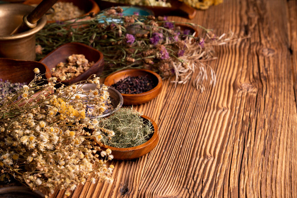 Natural medicine background. Assorted dry herbs in bowls and brass mortar on rustic wooden table. - Фото, зображення