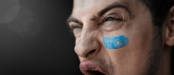 A screaming man with the image of the International Intellectual Property Organization national flag on his face - Фото, изображение
