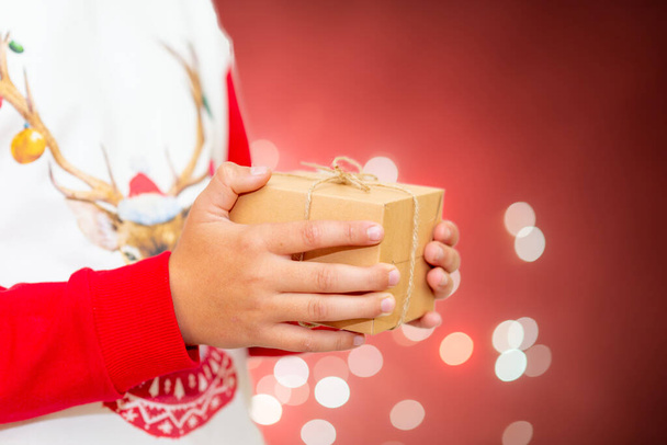 Young boy hand holding gift box.Festive fireworks colorful display red background.Beautiful light for celebration.Happy new year 2022 wallpaper. - Foto, imagen