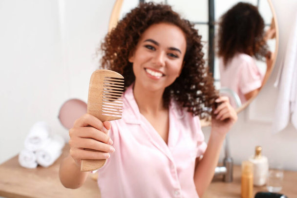 Young African-American woman with wooden comb in bathroom - Foto, immagini