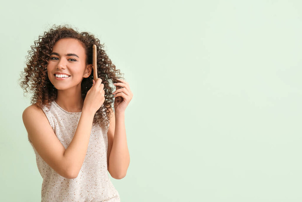 Young African-American woman combing her hair on green background - Foto, Imagem