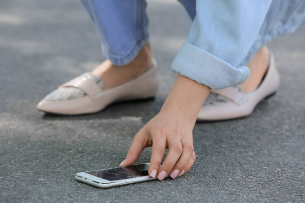 Vrouw plukken beschadigde mobiele telefoon van de stoep buiten, close-up - Foto, afbeelding