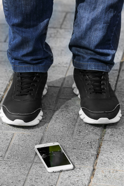 Pernas do homem e telefone celular danificado no pavimento ao ar livre, close-up - Foto, Imagem