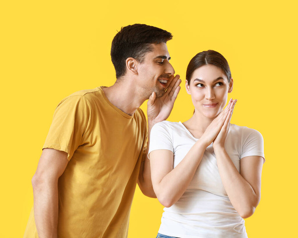 Young man sharing gossip with his wife on yellow background - Photo, Image