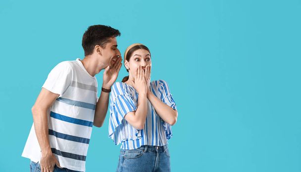 Νεαρός άνδρας μοιράζεται κουτσομπολιά με την κοπέλα του σε μπλε φόντο - Φωτογραφία, εικόνα