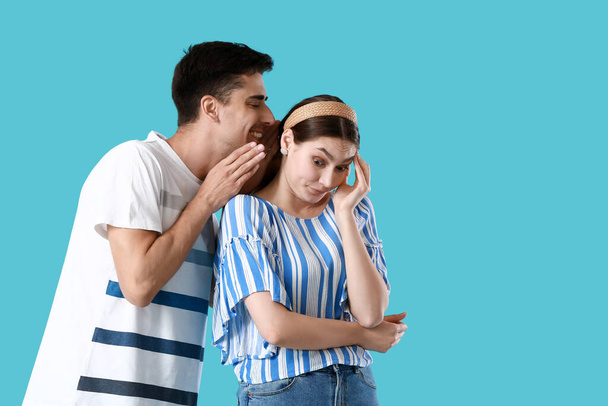 Nuori mies jakaa juoruja tyttöystävänsä kanssa sinisellä taustalla - Valokuva, kuva