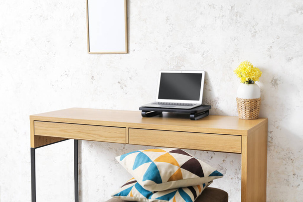 Laptop i kwiaty w wazonie na drewnianym biurku w pobliżu ściany światła - Zdjęcie, obraz