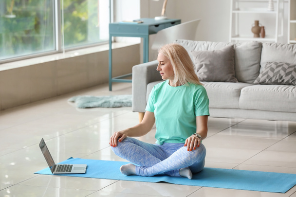 Beautiful mature woman meditating with laptop at home - Foto, Imagen