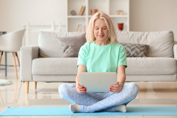 Gyönyörű érett nő használja laptop edzés közben otthon - Fotó, kép