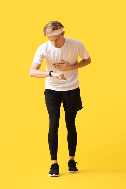 Sporty male runner checking pulse on color background - Foto, imagen