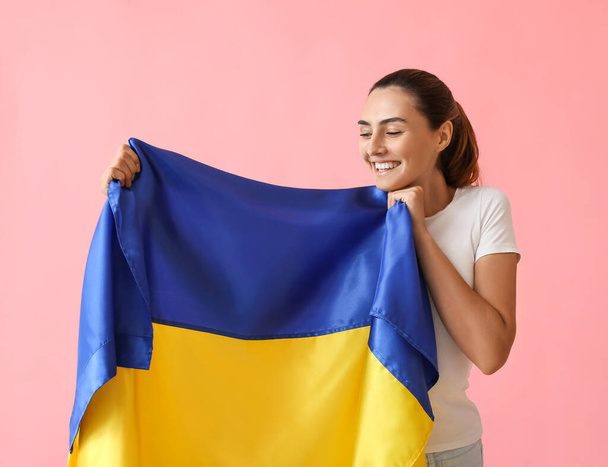 Happy young woman with Ukrainian flag on color background - Photo, image