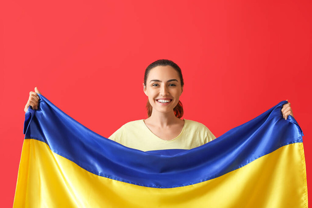 Happy young woman with Ukrainian flag on color background - Foto, afbeelding