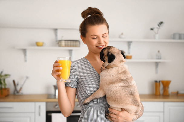 Young woman with cute pug dog and glass of juice in kitchen - Photo, Image