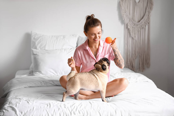 Joven mujer jugando con lindo perro pug en el dormitorio - Foto, Imagen