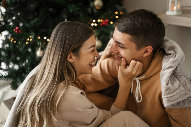 Nettes junges Paar sitzt neben geschmücktem Weihnachtsbaum und hat Spaß zusammen. Winterurlaub - Foto, Bild