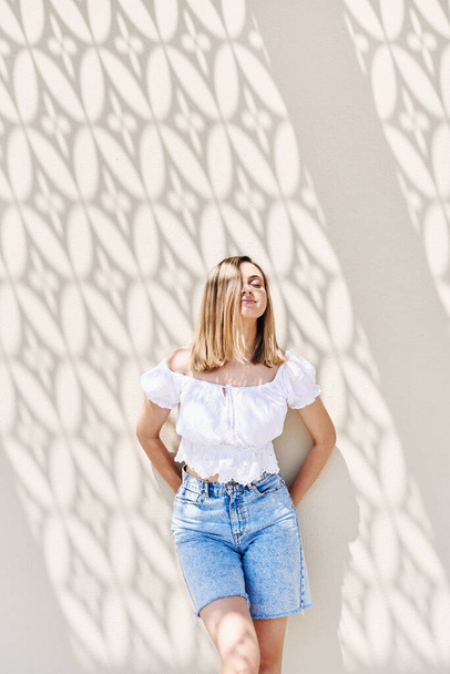 Muotokuva nuoresta vaaleasta naisesta, joka seisoo seinän lähellä kauniiden varjojen kanssa. Kesäkaudella. Onnellisuus ja naisellisuus käsite - Valokuva, kuva