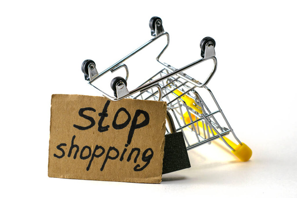 kohtuullisen kulutuksen epäämisen käsite on käänteinen ostoskärry, jossa on riippulukko ja kyltti, jossa on merkintä "stop shopping" valkoisella pohjalla. Laadukas kuva - Valokuva, kuva