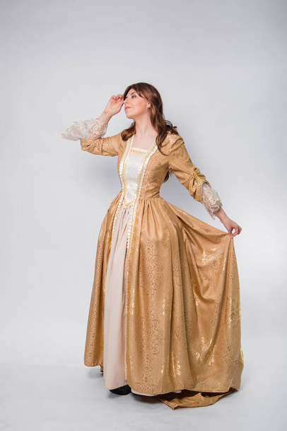 A full-length portrait of a girl in a golden rococo gown posing isolated on a white background. - Фото, изображение