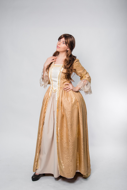 A full-length portrait of a girl in a golden rococo gown posing isolated on a white background. - Photo, image
