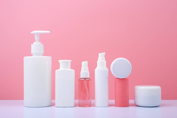 Trendy modern composition with a set of beauty products in white tubes in a row against on white table pink background. Concept of daily skin care routine  - 写真・画像