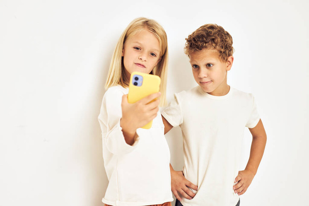 Imagen de niño y niña sonriendo con el teléfono en la mano fondo de luz de la moda - Foto, Imagen