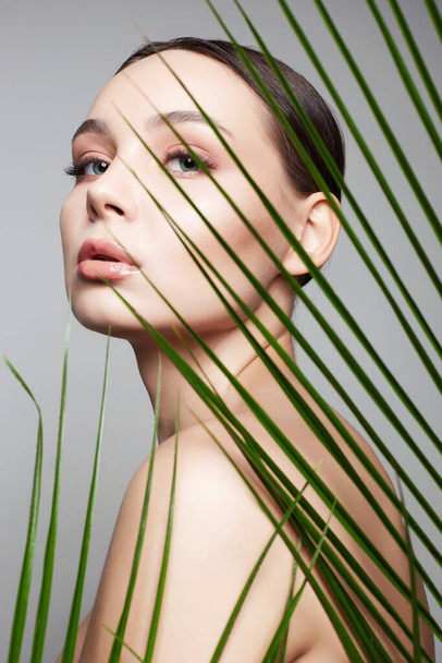 красивая девушка в пальмовых листьях. Красивая молодая женщина с макияжем. Портрет красавицы. Естественная косметика - Фото, изображение