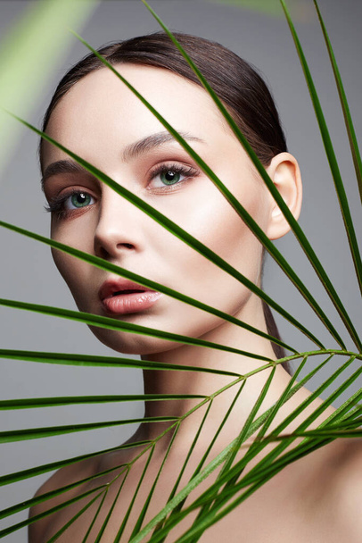 Piękna dziewczyna w liściach palmowych. Piękna młoda kobieta z makijażem. Piękny portret. Kosmetyki naturalne - Zdjęcie, obraz