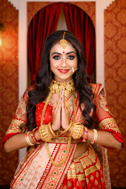 Portret bardzo pięknej młodej hinduskiej damy w luksusowym stroju z makijażem i ciężką biżuterią pozowanie modne w studio oświetlenia wewnątrz. Religijny styl życia Moda świąteczna. - Zdjęcie, obraz