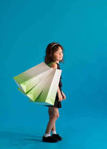 Girl in black dress with paper bags go shopping for discounts on blue background - Фото, зображення