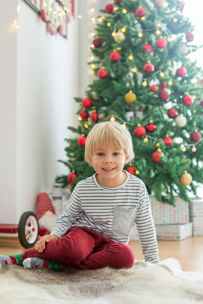 Beautiful toddler child, sitting in front of  Christmas tree, decoration and presents around him - Valokuva, kuva