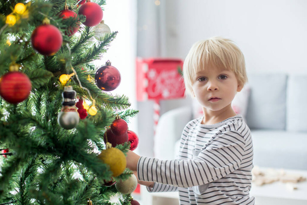 Beautiful toddler child, decorating   Christmas tree at home, presents under the trees - Foto, Bild