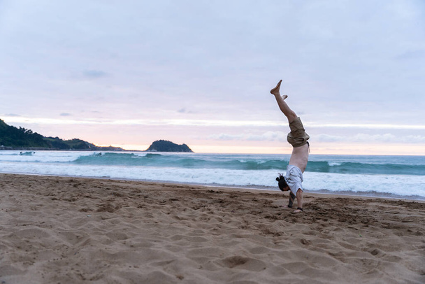 Young man doing a handstand in the beach during sunset, concept of yoga - Foto, Bild