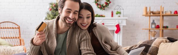 jókedvű férfi kezében hitelkártya közelében mosolygós feleség díszített nappaliban, banner - Fotó, kép