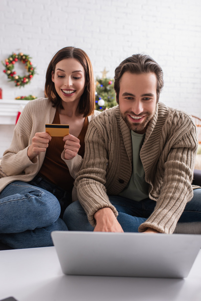 homem feliz usando laptop perto da esposa com cartão de crédito na sala de estar - Foto, Imagem
