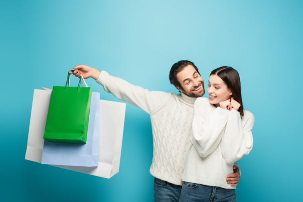 hombre sosteniendo bolsas de compras y abrazando a la mujer feliz en azul - Foto, imagen