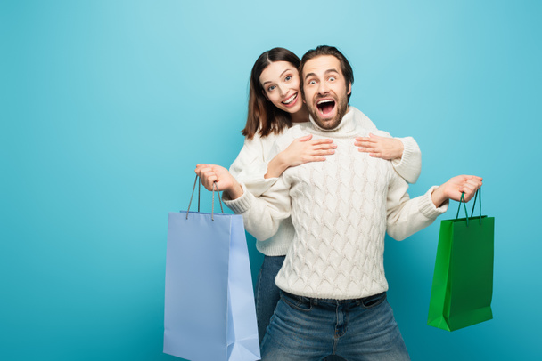 happy woman hugging thrilled man holding purchases on blue - Photo, Image