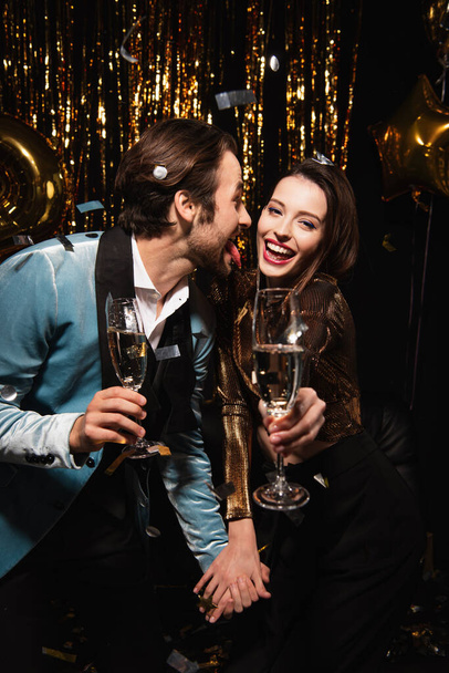 man sticking out tongue near cheerful woman during christmas party on black - Photo, Image