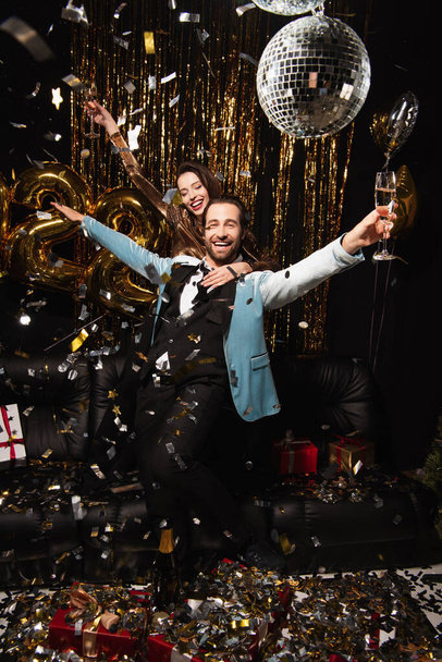 couple excité avec verres à champagne dans les mains tendues près de la décoration brillante sur noir - Photo, image