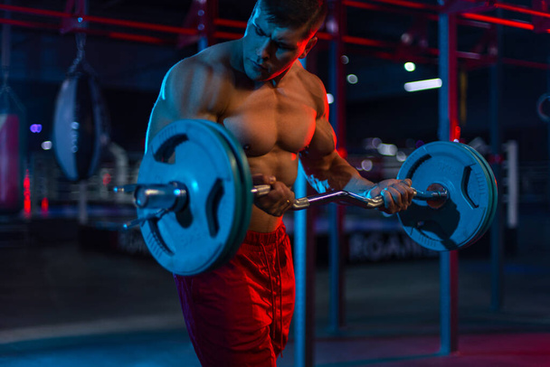 Bodybuilder athlete man pumping up muscles in the gym. Brutal strong muscular guy on fitness workout. Bodybuilding concept. - 写真・画像